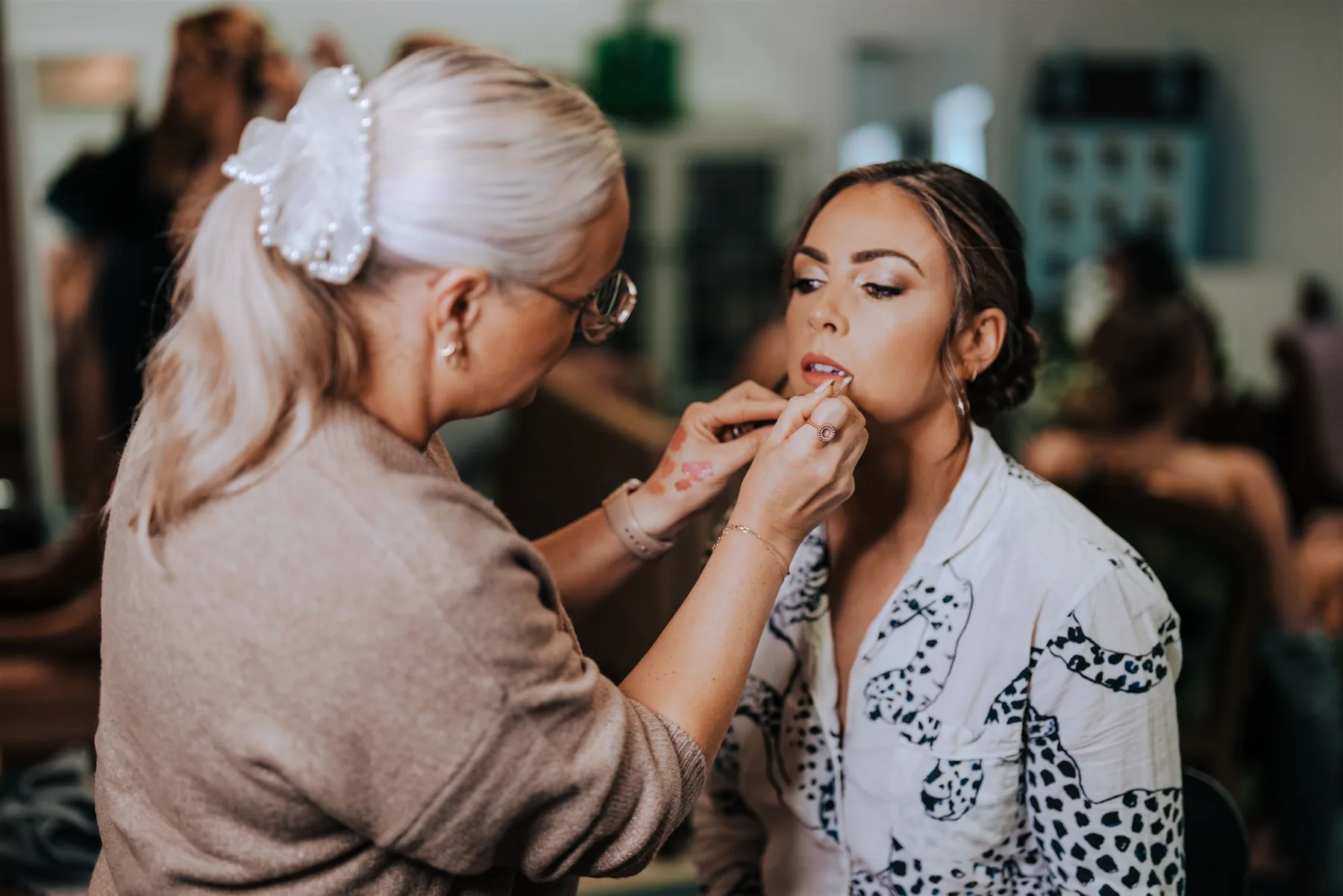 Anna Fullbrook applying lip colour to a client in a patterned shirt in a busy getting-ready room