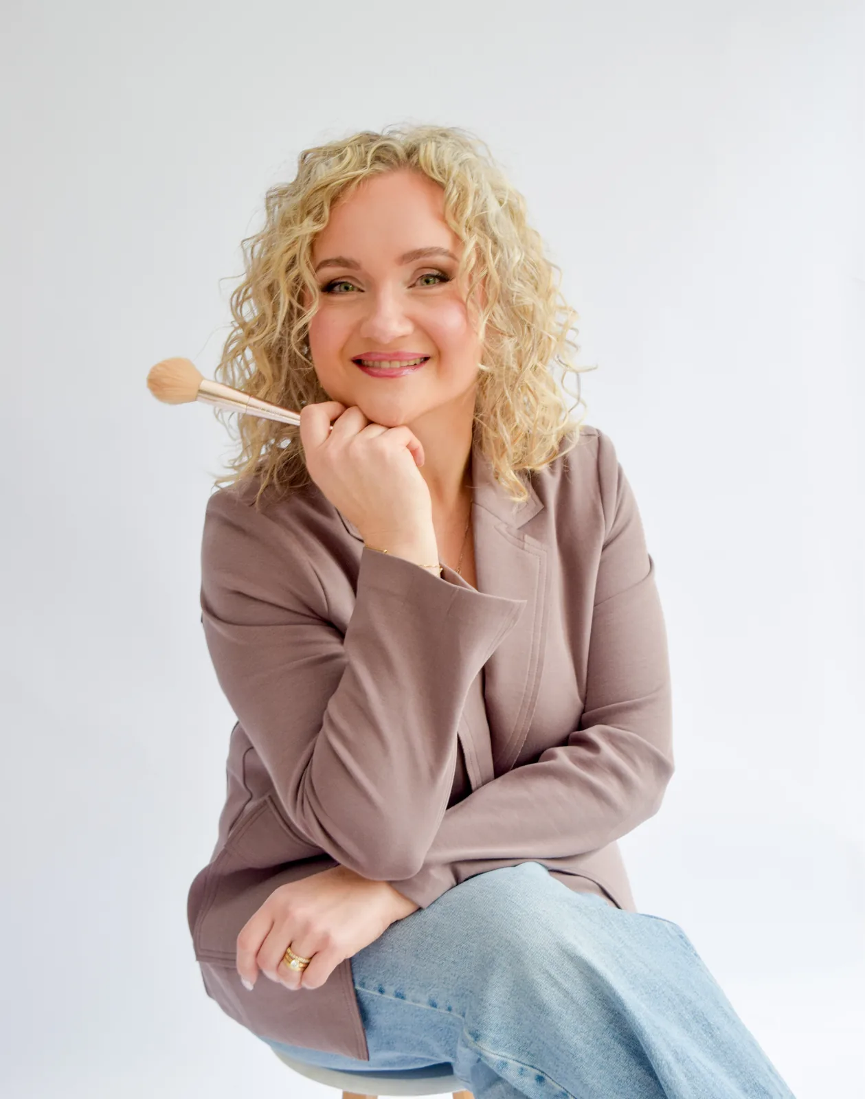 Anna Fullbrook holding a makeup brush, resting her chin on her hand and smiling