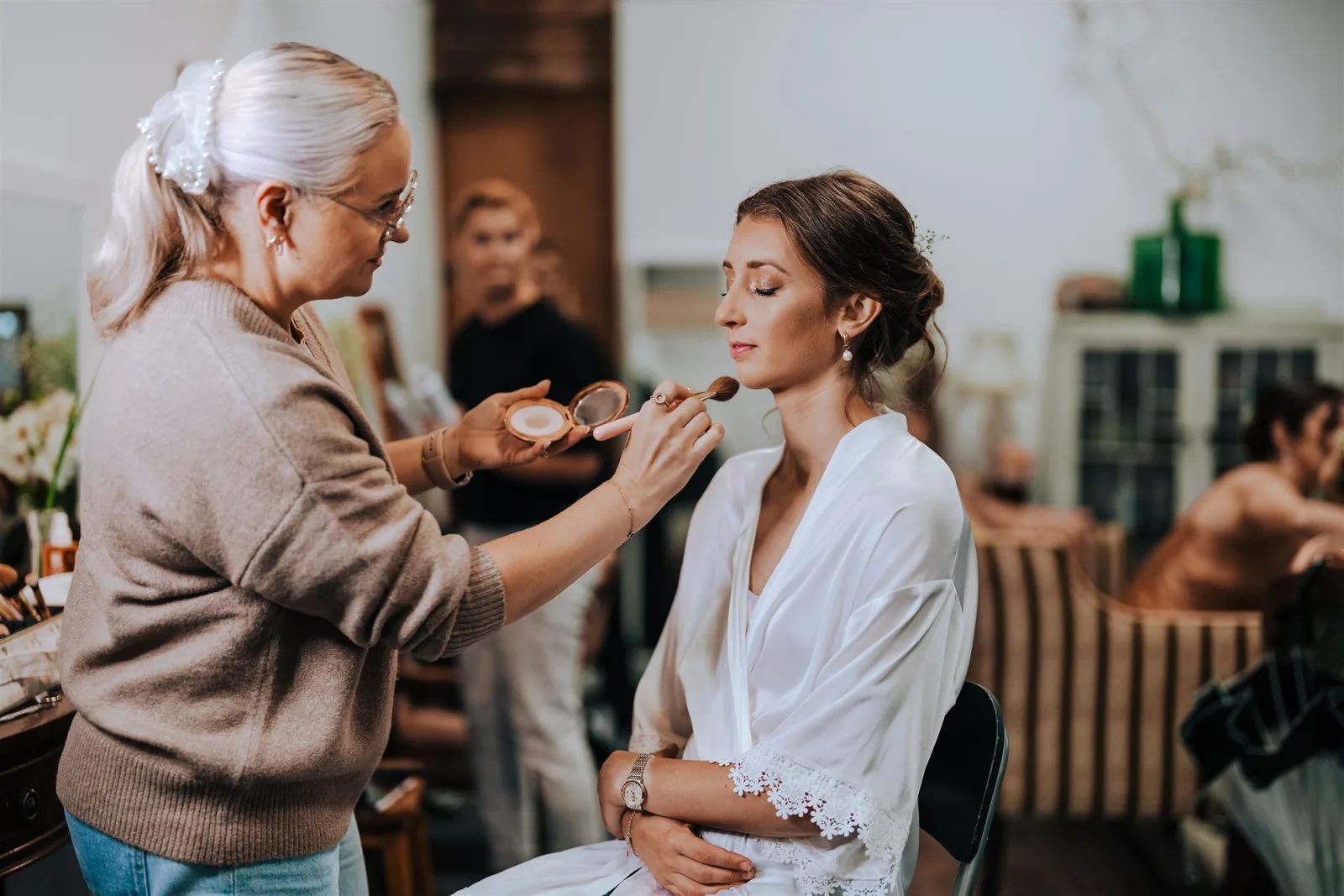 Anna applying makeup to a bride in a busy getting-ready room