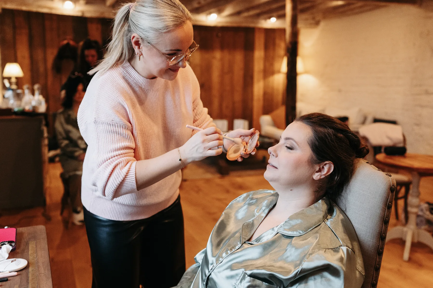Anna Fullbrook applying makeup to a relaxed client in a warm, busy getting-ready room