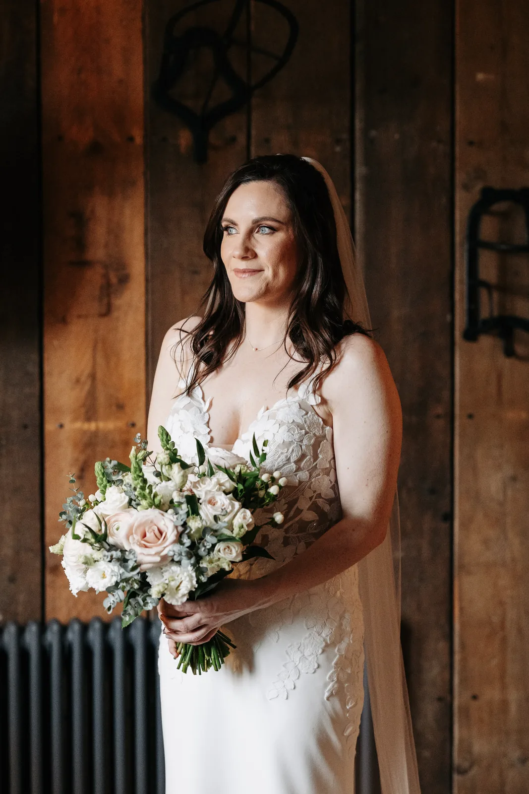 A bride with her bouquet in a timber doorway, wearing natural bridal makeup