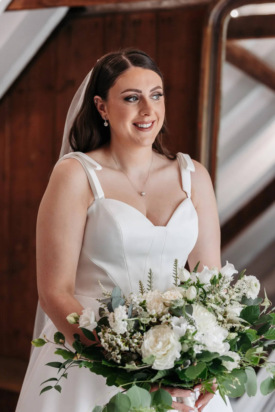 A smiling bride holding a white bouquet, wearing soft bridal makeup
