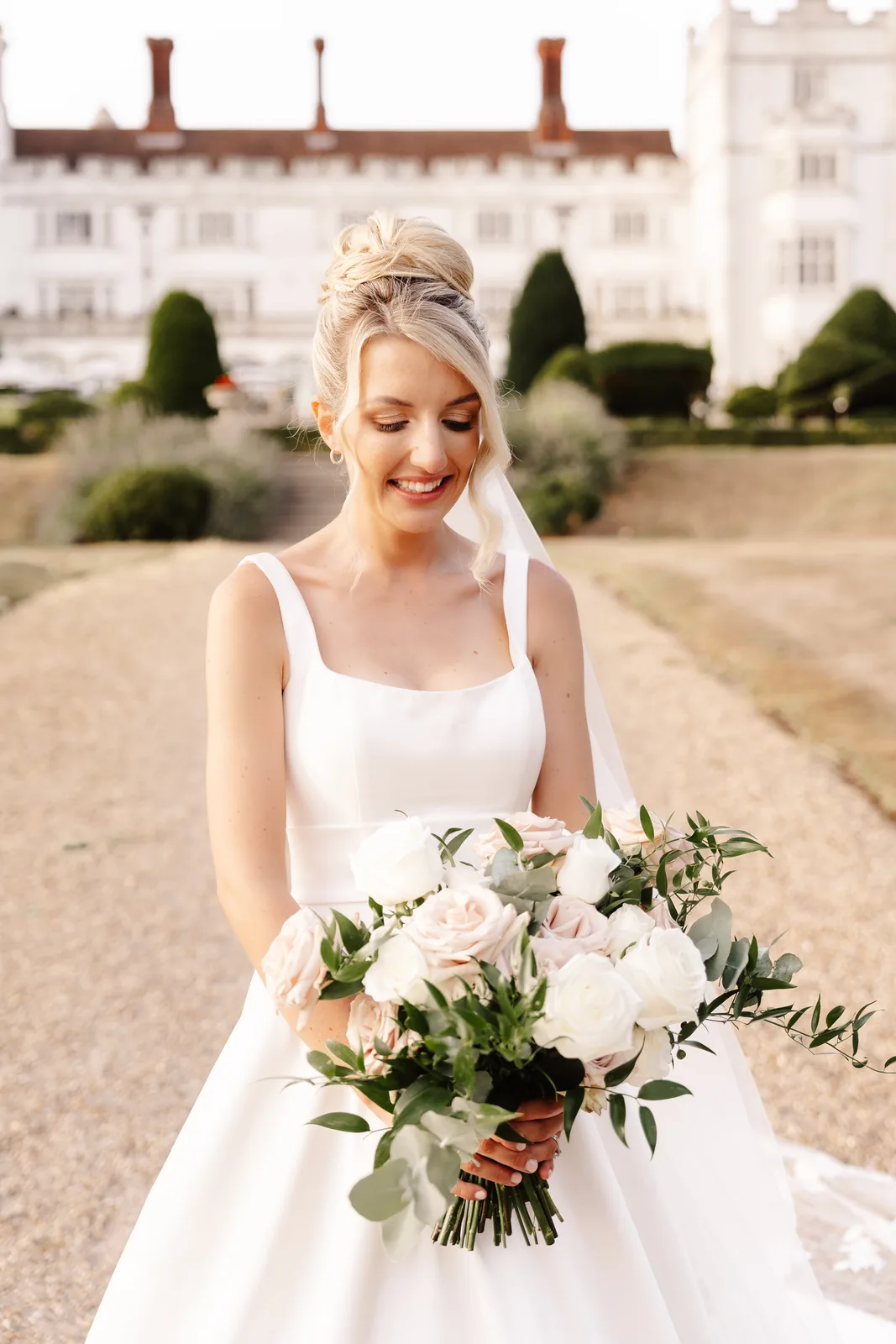 A bride looking down at her bouquet in a garden, wearing bridal makeup