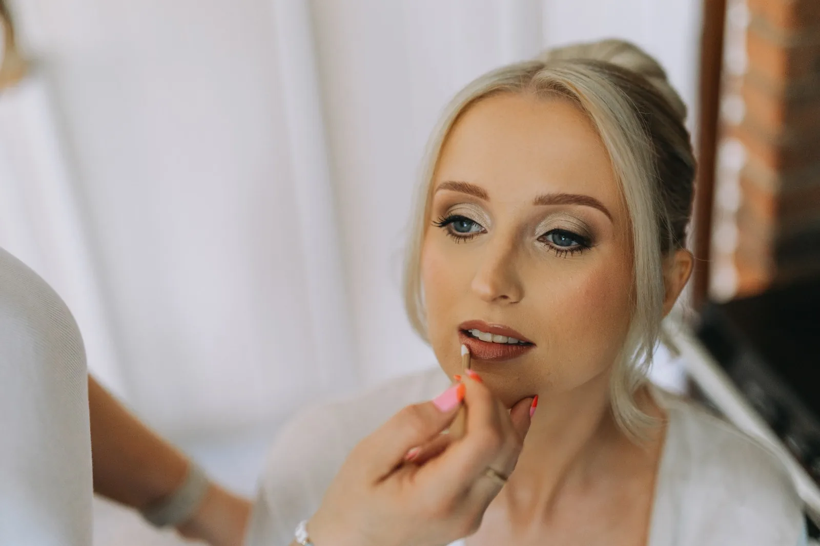 Lip colour being applied to a bride with bronzed eye makeup, close up