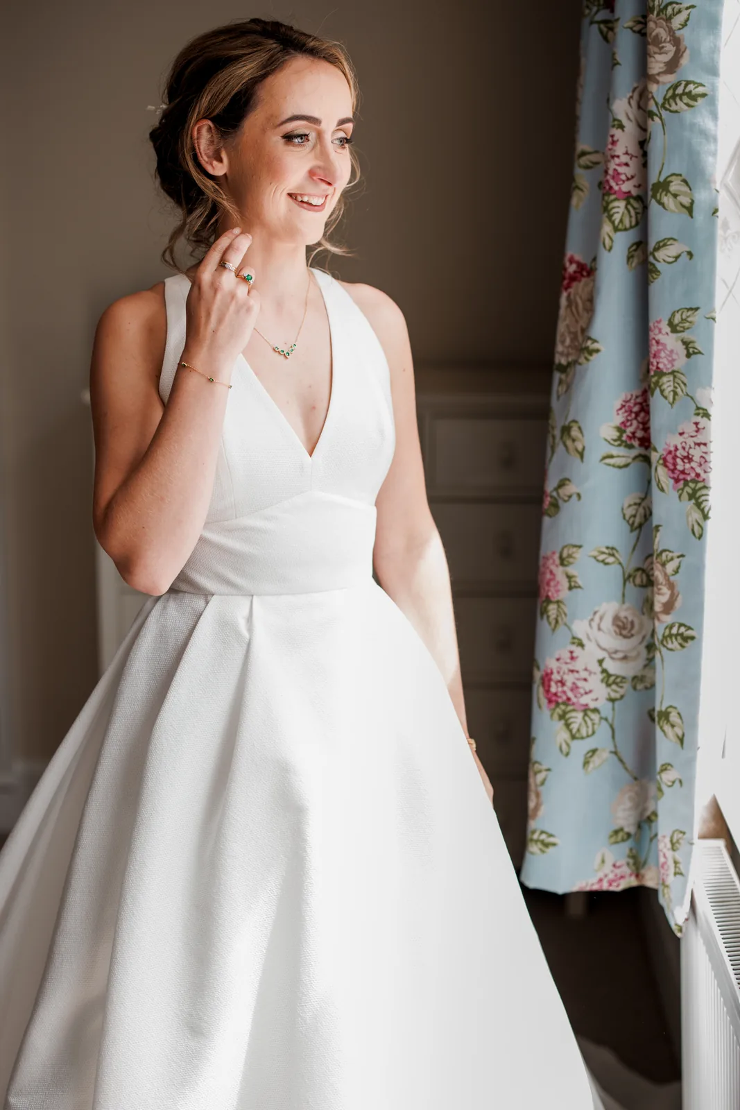 A bride by a window in natural light, wearing fresh bridal makeup