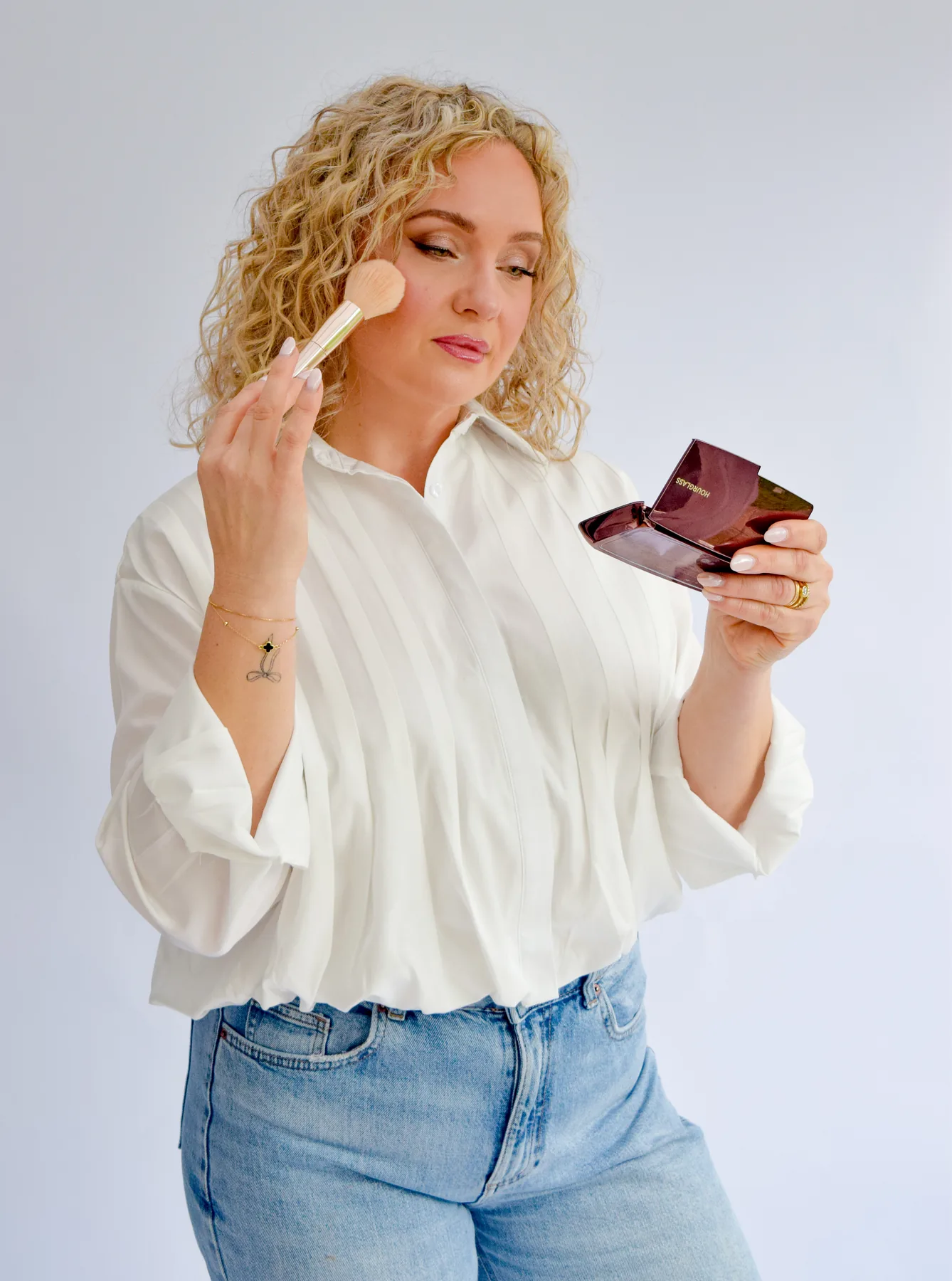 Anna Fullbrook demonstrating blush placement on her own cheek with a brush and compact