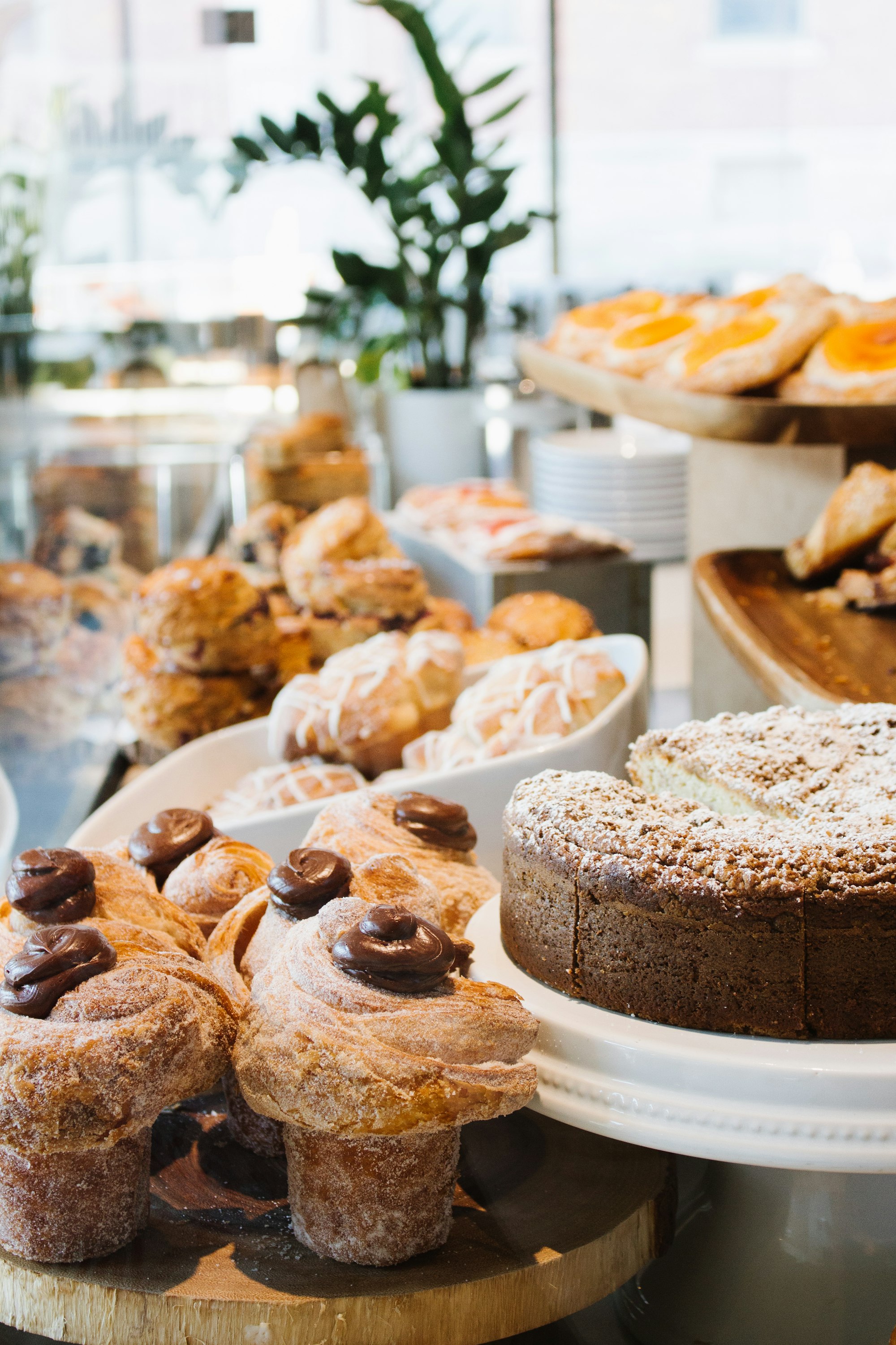 Cruffins, glazed pastries and a crumb cake displayed on a sunlit café counter