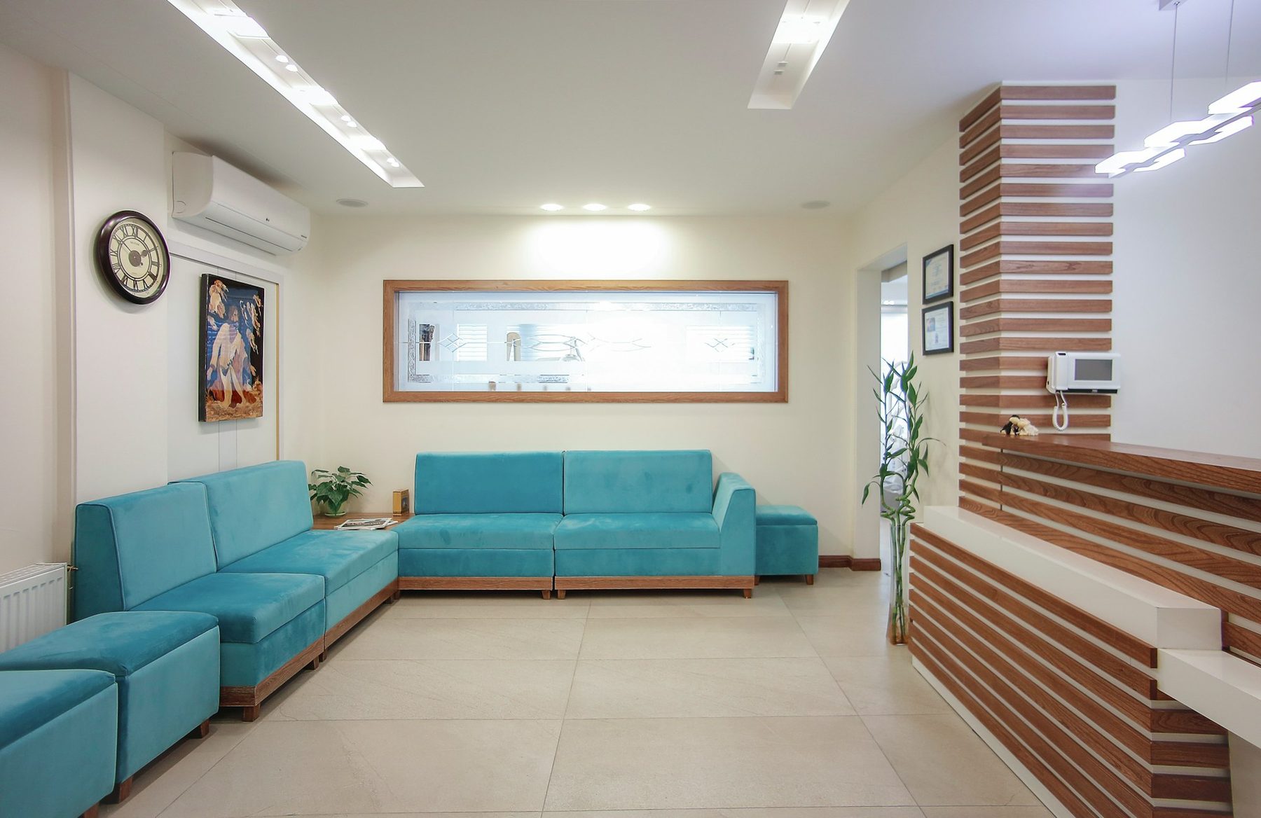 A bright practice waiting area with teal sofas, a plant and a wooden reception desk