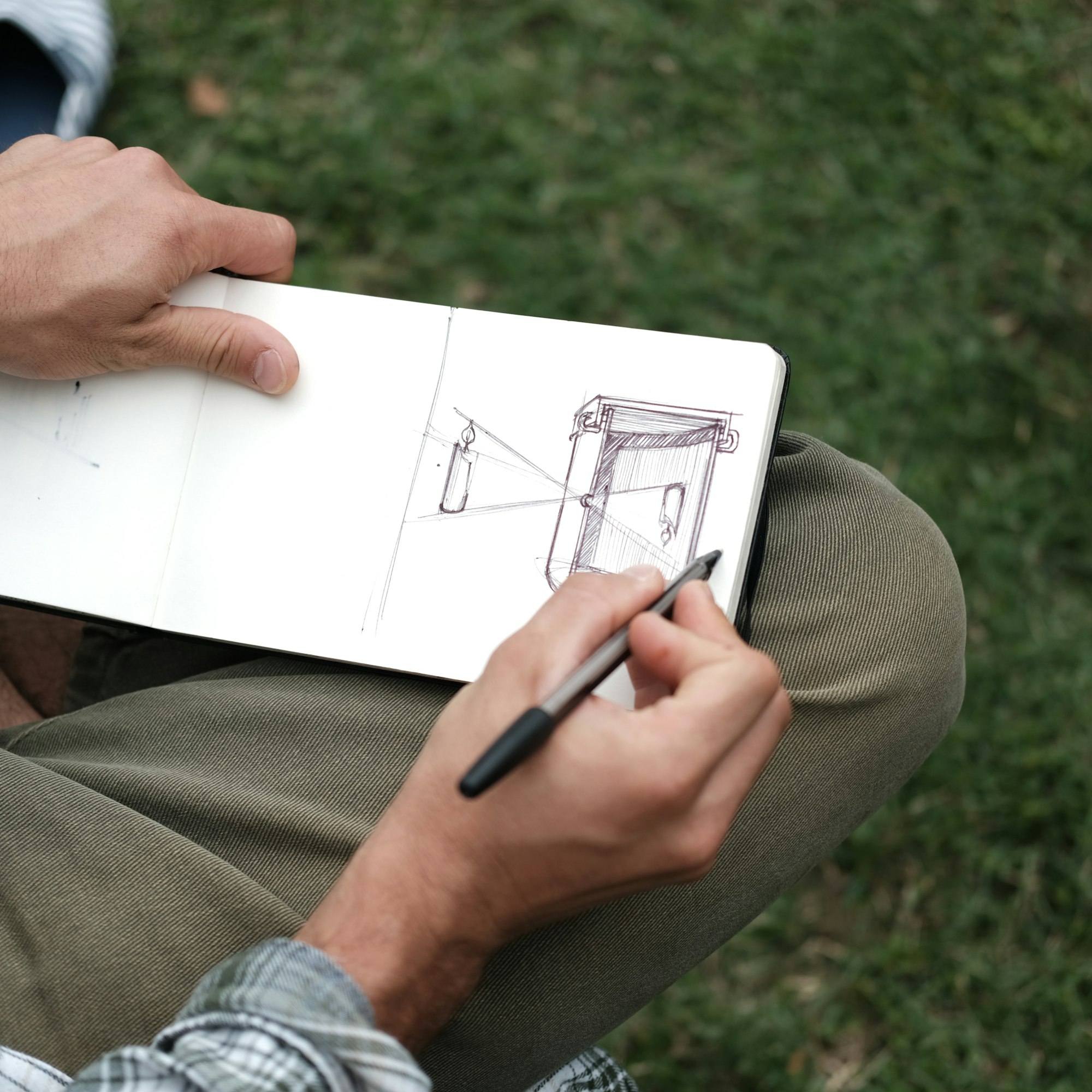 A designer sketching in a pen notebook while seated on a lawn