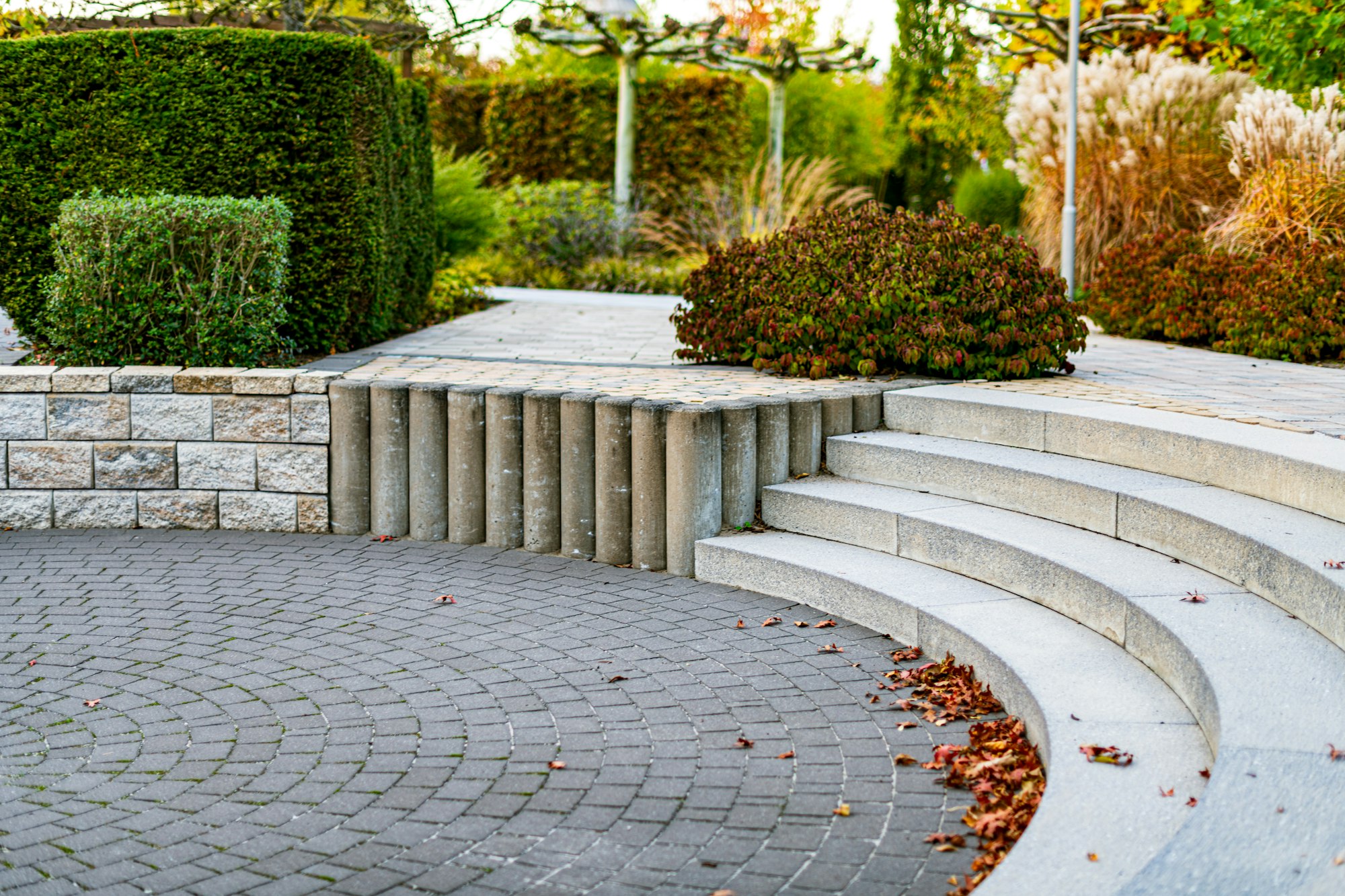 Curved stone steps and a circular paved terrace edged with clipped yew and autumn shrubs