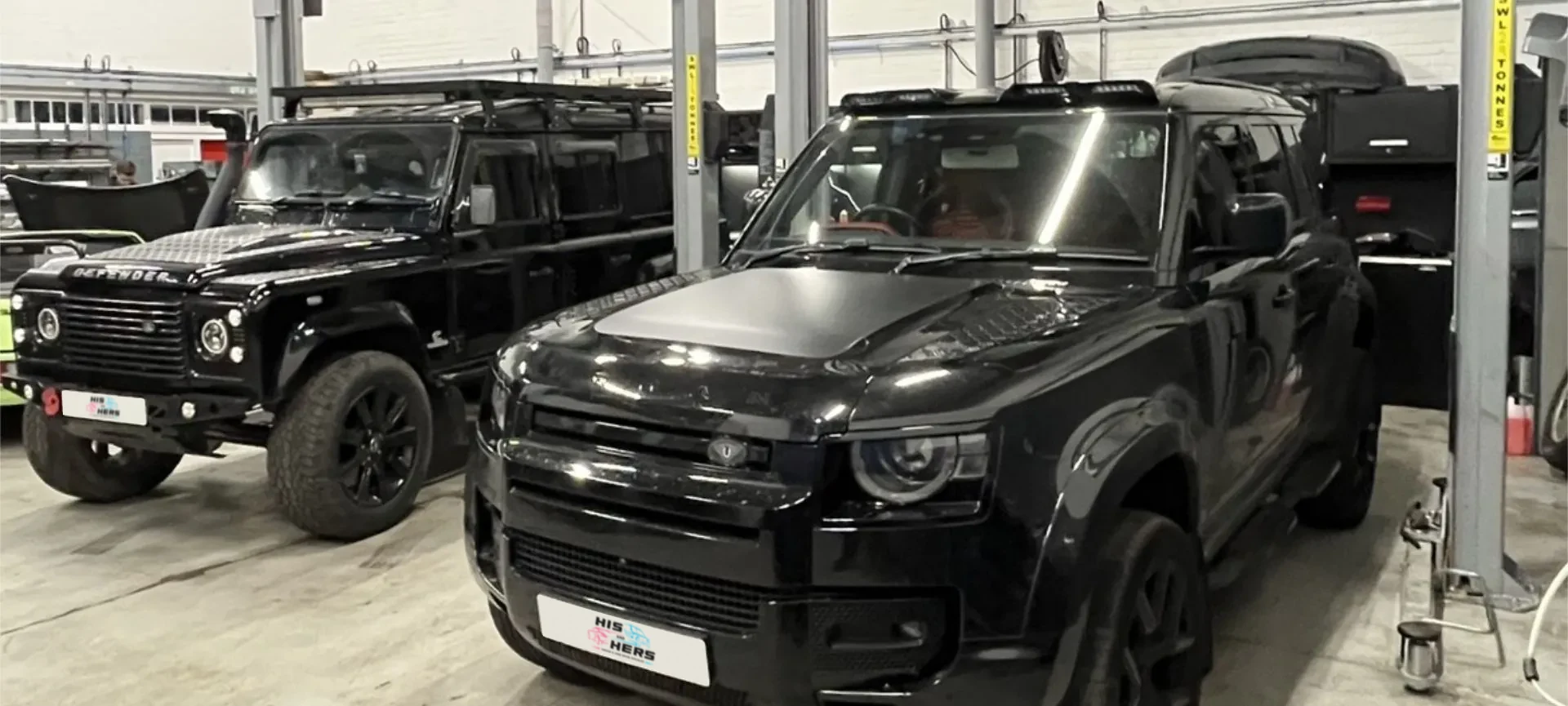 Two black Land Rover Defenders in the His and Hers Motors workshop