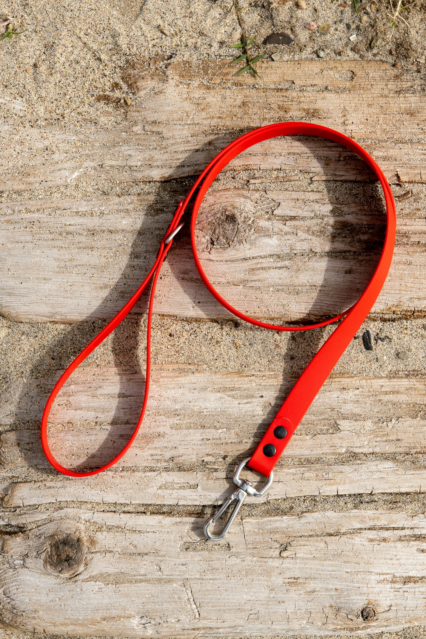 A bright red dog lead looped across weathered wooden boards